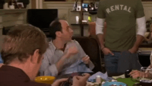 a group of men are sitting around a table with a man wearing a green rental shirt .