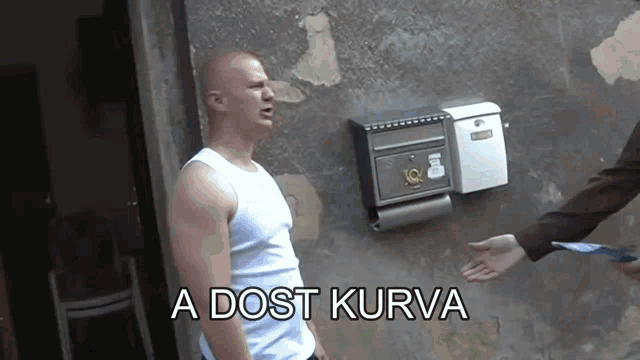 a man standing in front of a wall with the words a dost kurva written below him