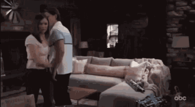 a couple standing next to each other in a living room with a couch and a fireplace .
