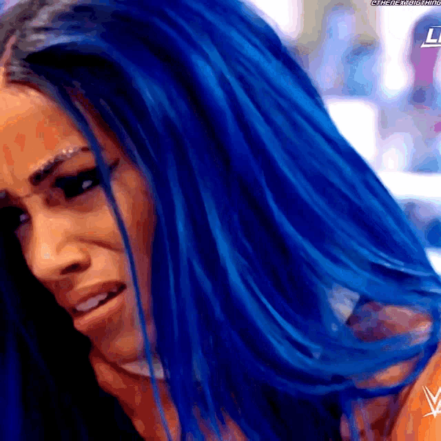 a close up of a woman 's face with blue hair and a w logo in the corner