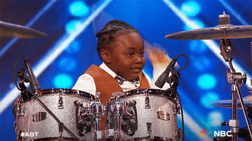 a young boy is playing drums on a stage with the nbc logo in the background