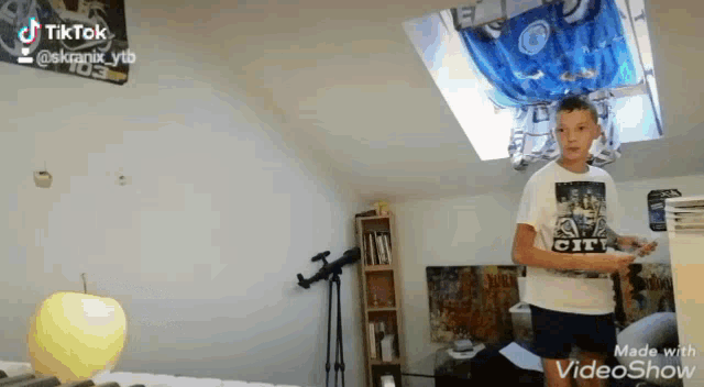 a boy in a white shirt with the word city on it is holding a remote control in a bedroom .