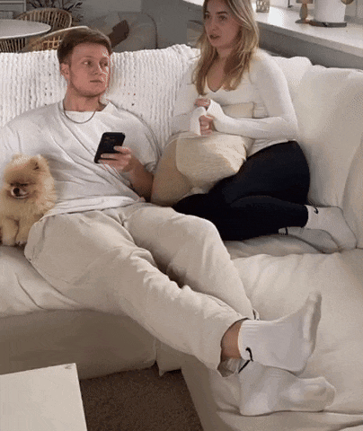 a man and woman sit on a couch with a dog