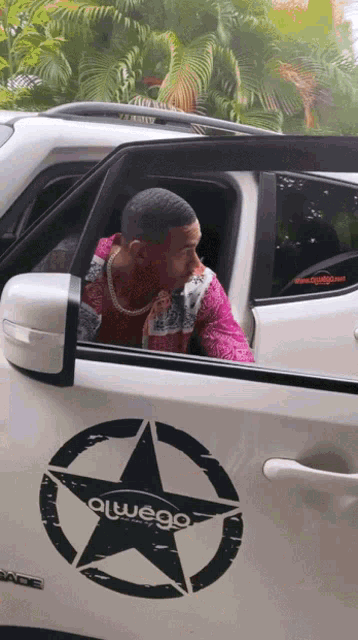 a man is sitting in the driver 's seat of a white car with a black star on the side that says alwego