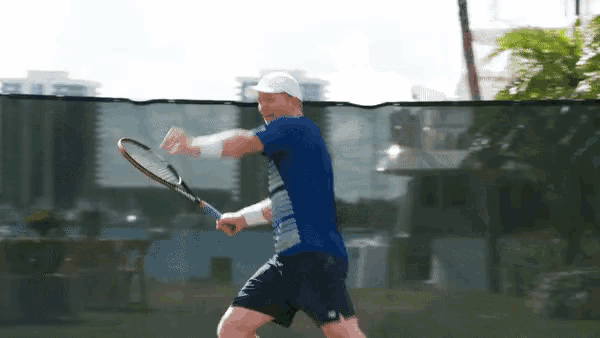 a man in a blue shirt and white hat is swinging a tennis racket