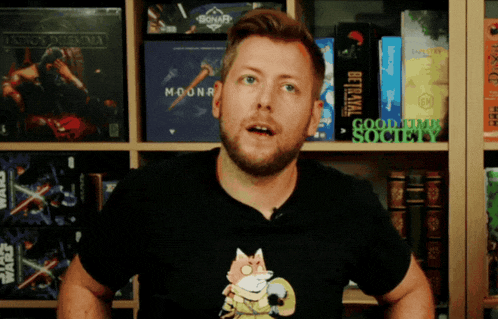 a man wearing a black shirt with a fox on it stands in front of a shelf full of games