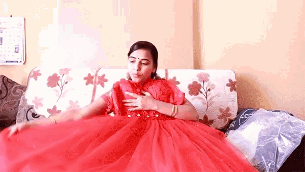 a woman in a red dress is sitting on a couch holding her dress .