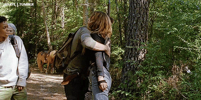 a woman is hugging another woman in the woods while a man watches .