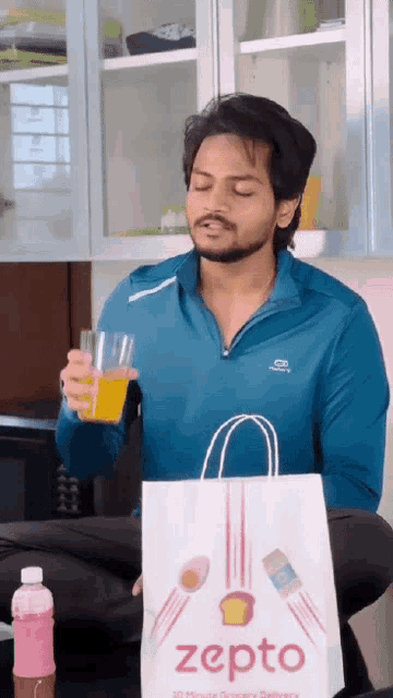 a man holding a glass of orange juice next to a bag that says zepto on it