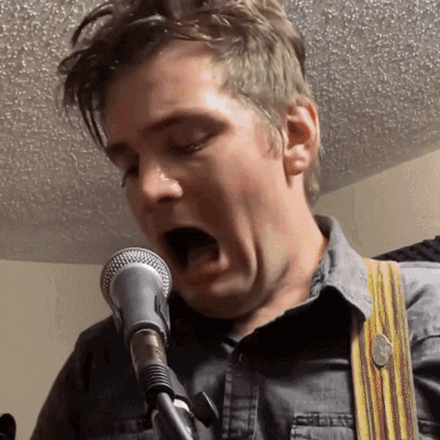a man is singing into a microphone with his mouth wide open