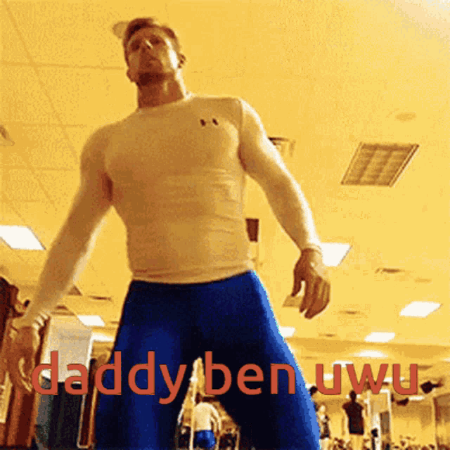 a man in a white shirt and blue shorts is standing in a gym with the words daddy ben uwu written in red