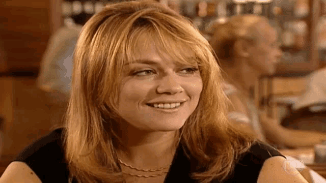a woman with long red hair is smiling while sitting at a table in a bar .