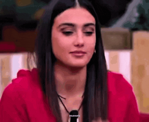 a woman is wearing a red hoodie and a black necklace and looking at the camera .