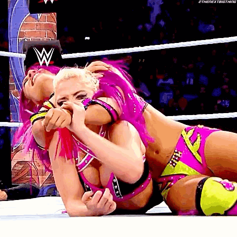 two women are wrestling in a wrestling ring and one of them has a w logo on her chest .