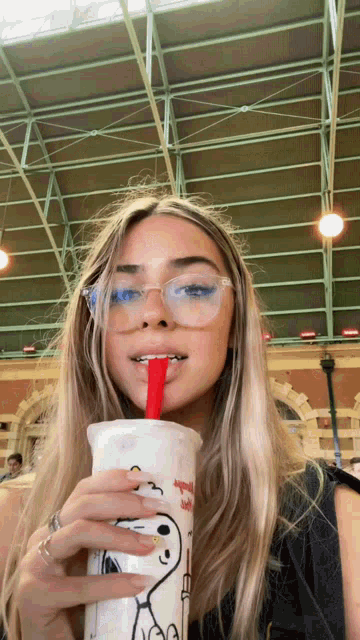 a woman with glasses is drinking from a snoopy cup