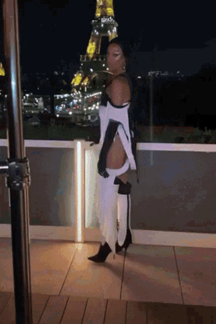 a woman standing on a balcony in front of the eiffel tower at night