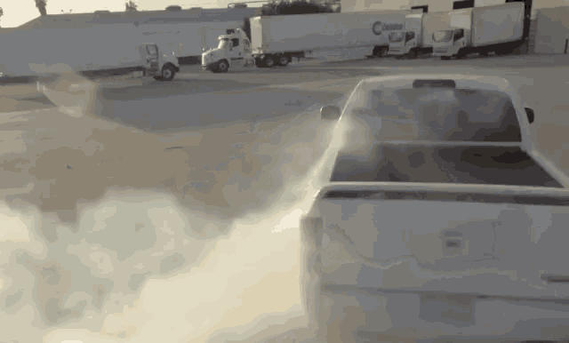 a white truck is drifting in a parking lot with smoke coming out of the tires .