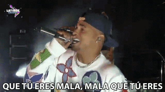 a man singing into a microphone with the words " que tu eres mala mala que tu eres " below him