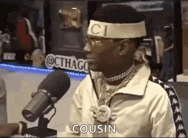 a man wearing a headband and glasses is talking into a microphone and saying `` cousin '' .