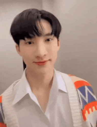 a young man wearing a white shirt and a colorful cardigan is looking at the camera .