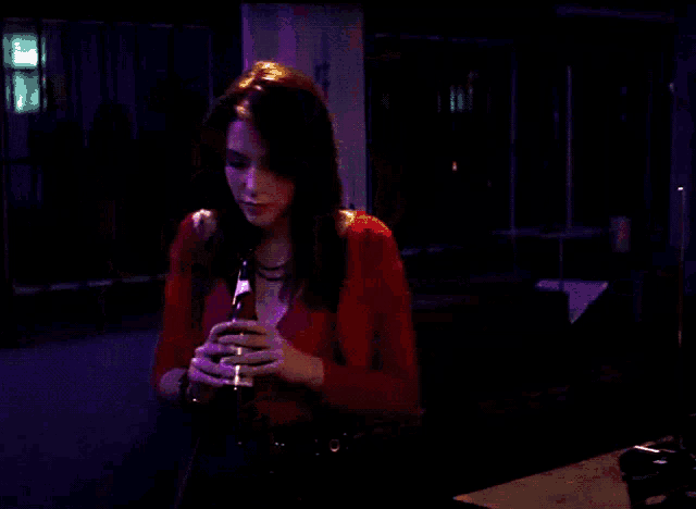 a woman in a red top is drinking from a bottle in a dark room