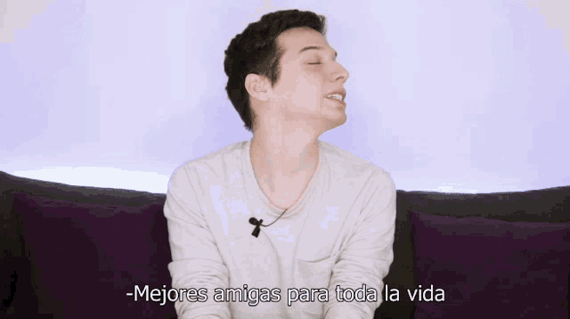a young man sitting on a couch with purple pillows says mejores amigas para toda la vida