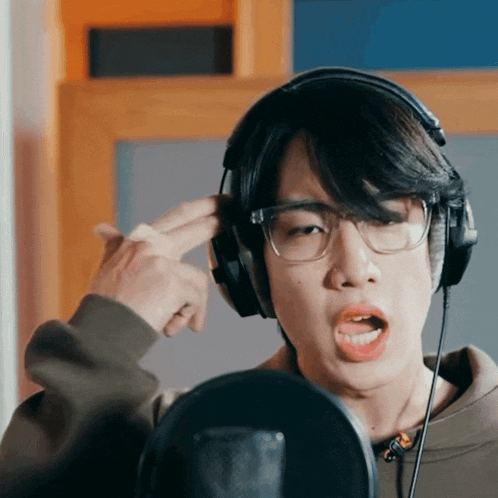 a young man wearing glasses and headphones sings into a microphone