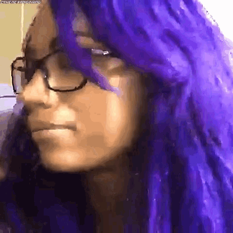 a woman with purple hair is wearing glasses and making a face .