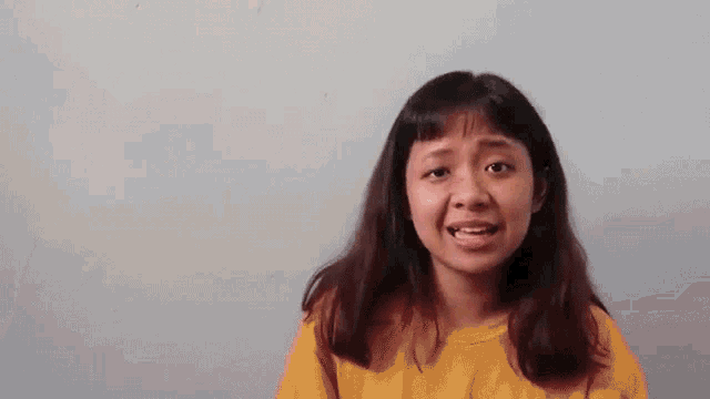 a young girl is smiling and making a funny face while wearing a yellow shirt .