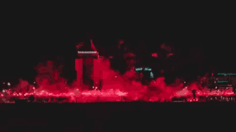 a crowd of people are gathered in front of a building with red smoke coming out of it ..