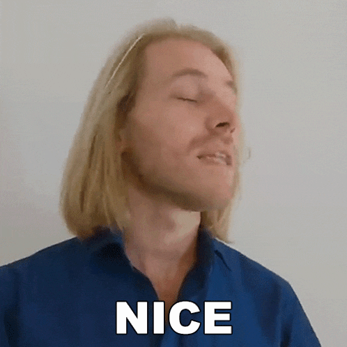 a man with long blonde hair and a blue shirt is smiling and saying nice .