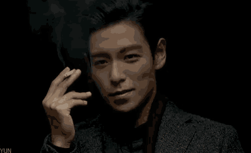 a young man in a suit is smoking a cigarette in a dark room .