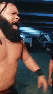 a shirtless wrestler with a beard is standing in a parking garage .