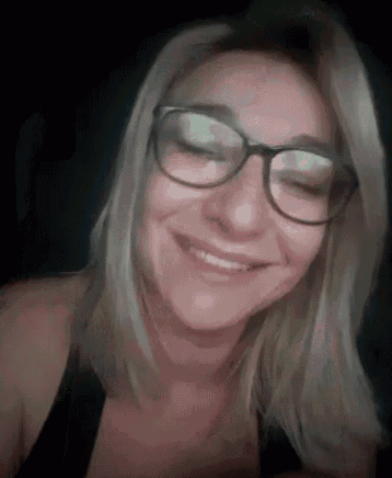 a woman wearing glasses and a black tank top is smiling .