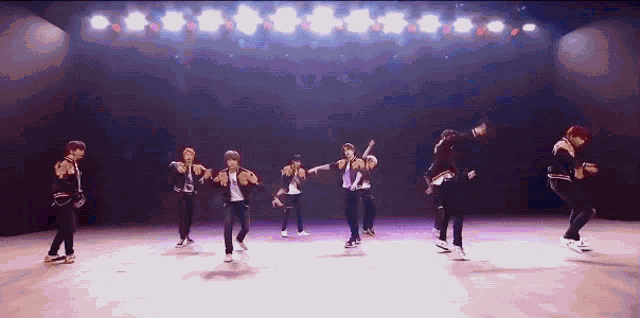 a group of young men are dancing on a stage in a dark room
