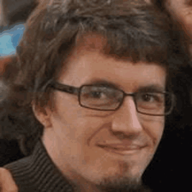 a man wearing glasses and a black sweater is smiling for the camera .
