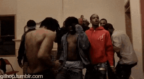 a group of men are dancing in a room . one of the men is wearing a red hoodie .