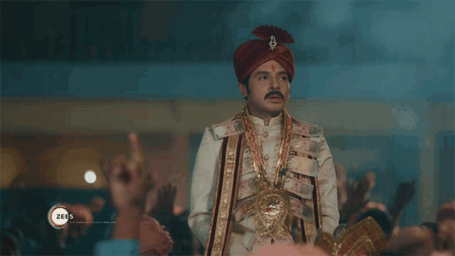 a man in a turban is standing in front of a crowd with a zee5 logo on the bottom right
