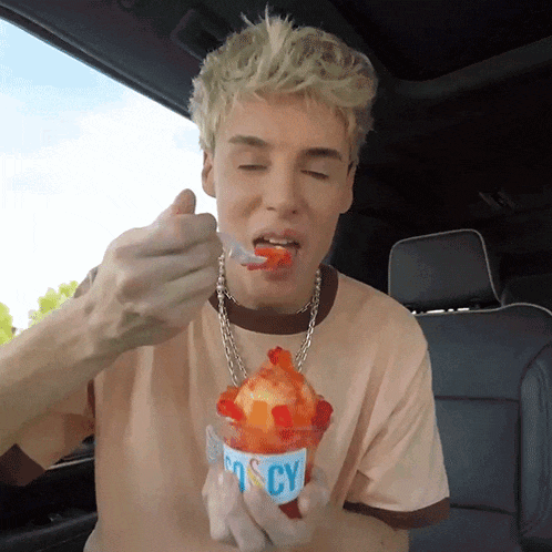 a man in a car is eating ice cream from a cup that says icy on it