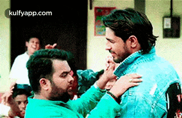 two men are hugging each other in a room with a crowd behind them .