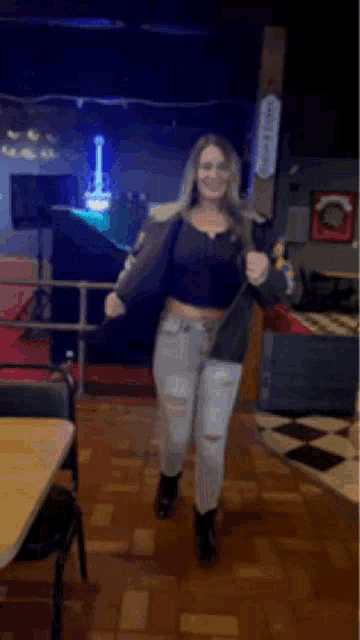 a woman in a crop top and jeans is dancing in a room with tables and chairs .