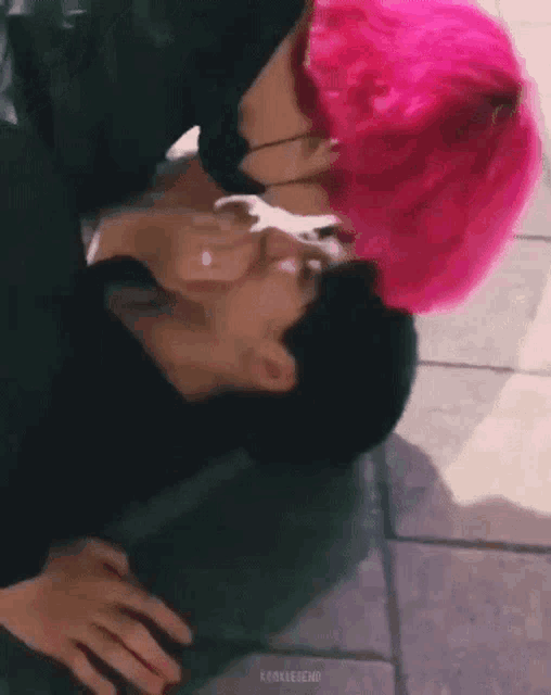 a couple of men with pink hair are kissing each other on the floor .