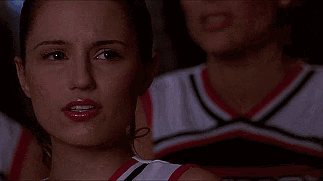 a close up of a woman 's face with a cheerleader behind her