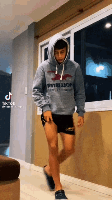 a man wearing a hoodie that says hollister is walking in front of a window
