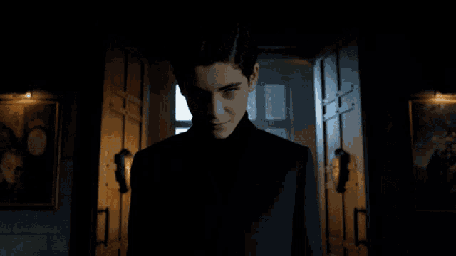 a man in a black suit stands in a dark hallway