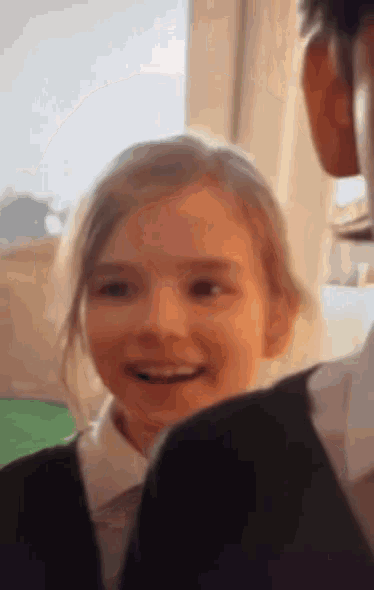 a little girl in a school uniform is smiling at the camera