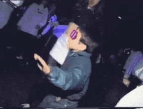 a young boy wearing a suit and sunglasses is dancing in a dark room .
