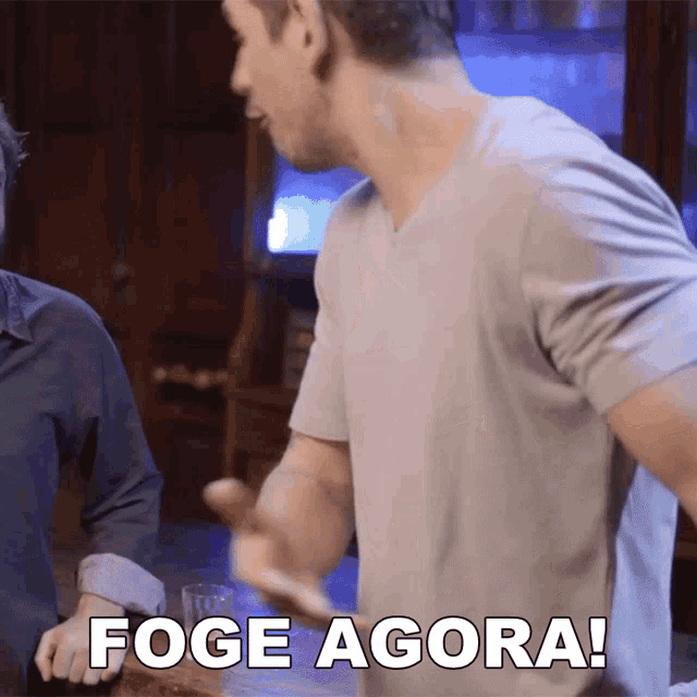 a man in a grey shirt says foge agora in a bar