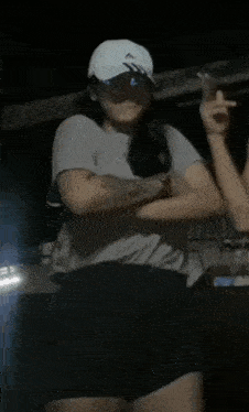 a woman wearing a hat and a t-shirt is dancing in the dark .
