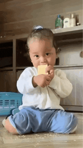 a baby is sitting on the floor and eating a piece of cheese .